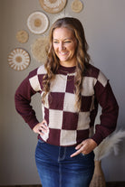 Front view of a brown and cream checkered sweater with solid long sleeves, worn with a denim skirt.