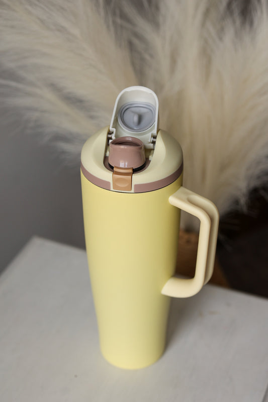 Yellow thermos with a white lid on a light surface, blurred fur in the background