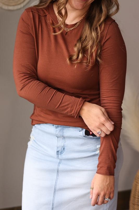 Person wearing a brown long-sleeve top and light blue denim skirt indoors for a cute fall winter top for women.
