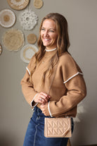 Angled front view of a deep camel stitch detail sweater styled with a small tan quilted shoulder bag.