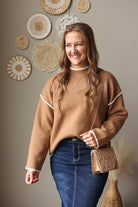 Camel knit sweater styled with a dark denim skirt, showing the mock neckline and contrast shoulder stitching.