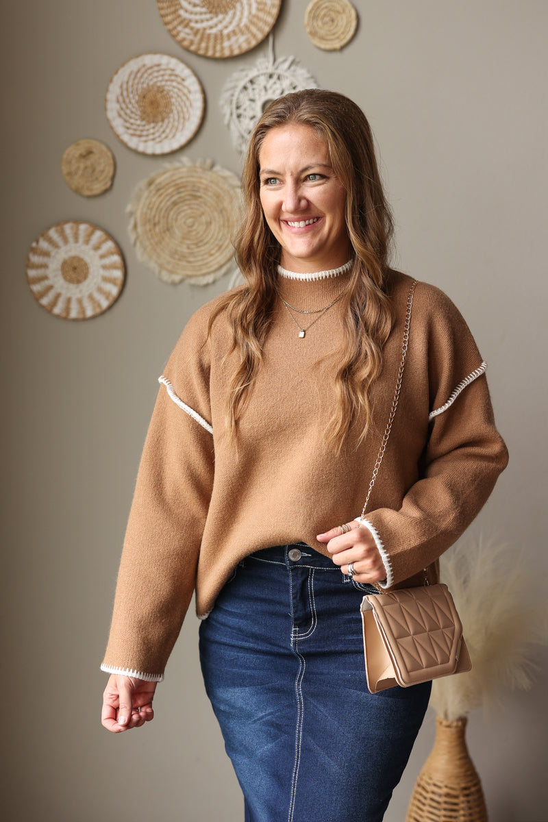 Camel knit sweater styled with a dark denim skirt, showing the mock neckline and contrast shoulder stitching.