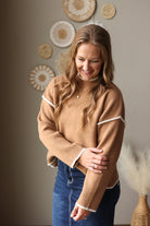 Close front view of a deep camel knit sweater highlighting the contrasting cuff stitching and long sleeves.