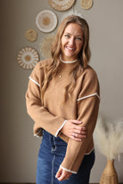 Close view of a camel sweater sleeve showing the ribbed cuff and contrasting light stitch trim.