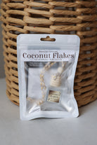 A Honey Jar Creations Coconut Flakes car oil diffuser in its white resealable packaging, positioned in front of a woven wicker basket.