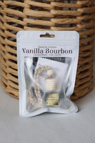 A Vanilla Bourbon car oil diffuser in its white retail packaging, placed in front of a woven wicker basket on a light gray surface.