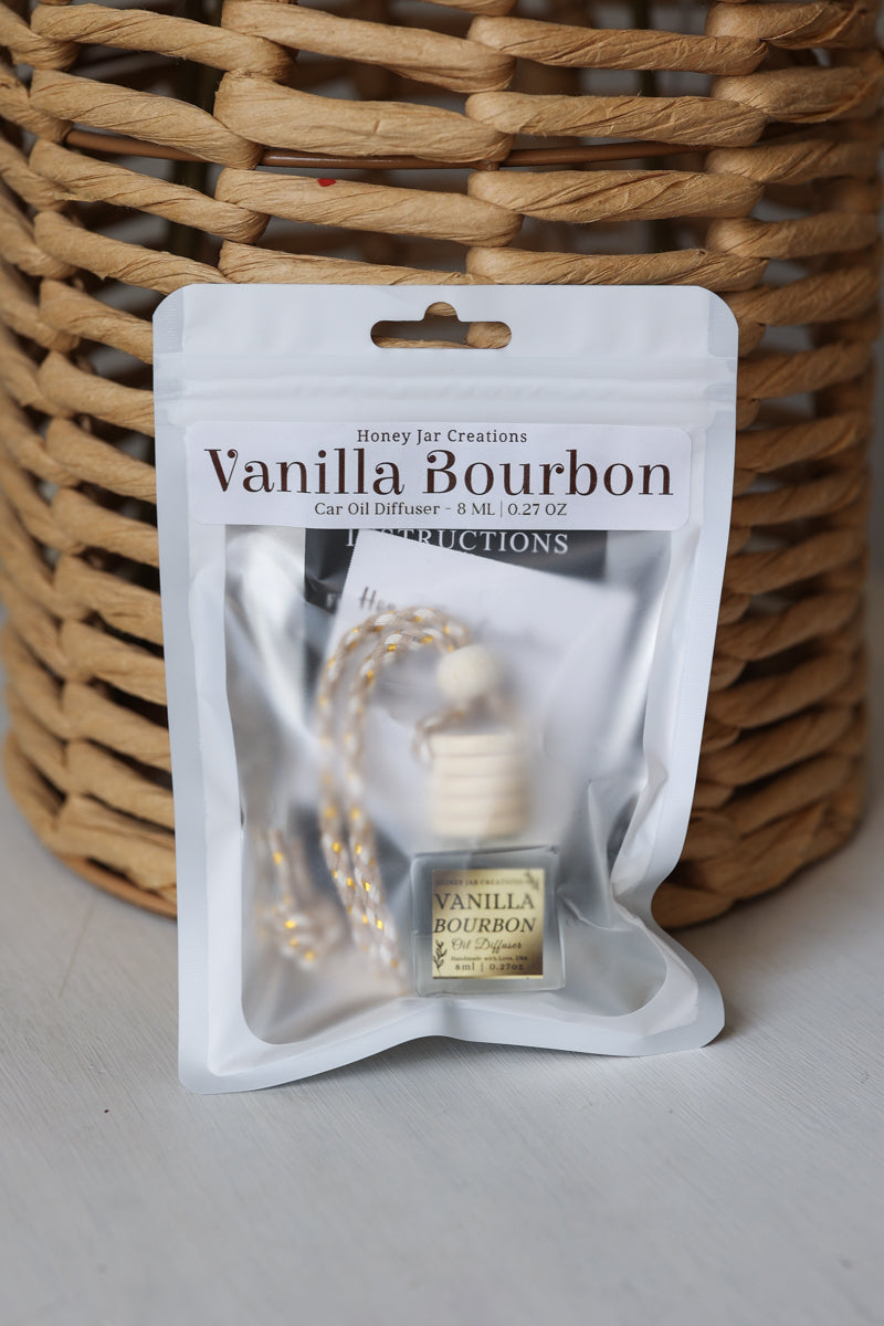 A Vanilla Bourbon car oil diffuser in its white retail packaging, placed in front of a woven wicker basket on a light gray surface.