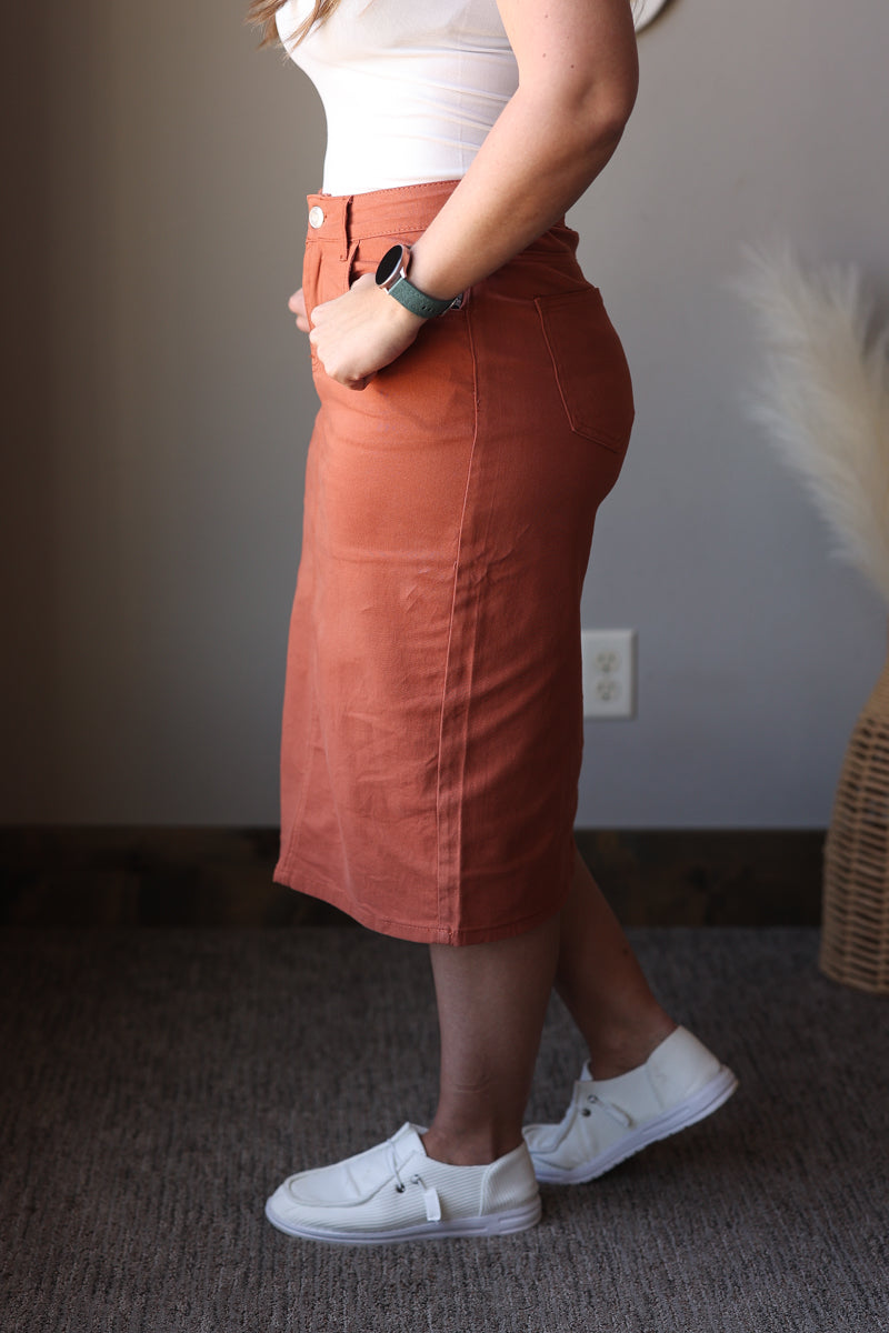 Person wearing a rust-colored skirt and white sneakers indoors.