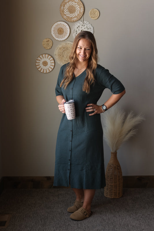Woman in a grey dress holding a coffee cup in a room with decorative wall art.