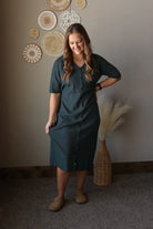 Woman in a gray dress standing in a room with decorative wall hangings.
