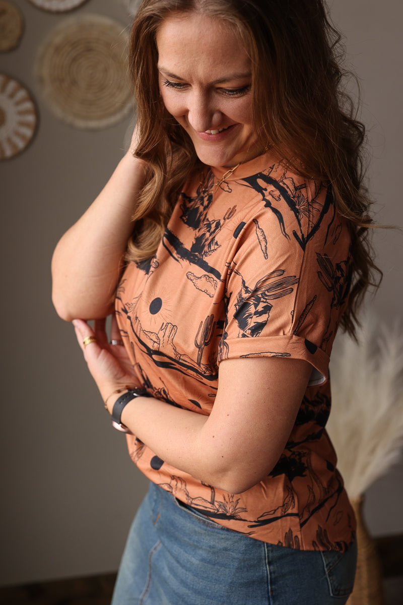 Woman wearing a patterned orange western t-shirt with black designs indoors.
