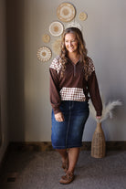 Full outfit view of a coffee brown plaid patchwork quarter zip sweatshirt with a denim midi skirt and brown boots.