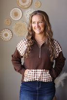Front view of a brown quarter zip sweatshirt with plaid shoulder panels and a contrasting plaid pouch pocket.