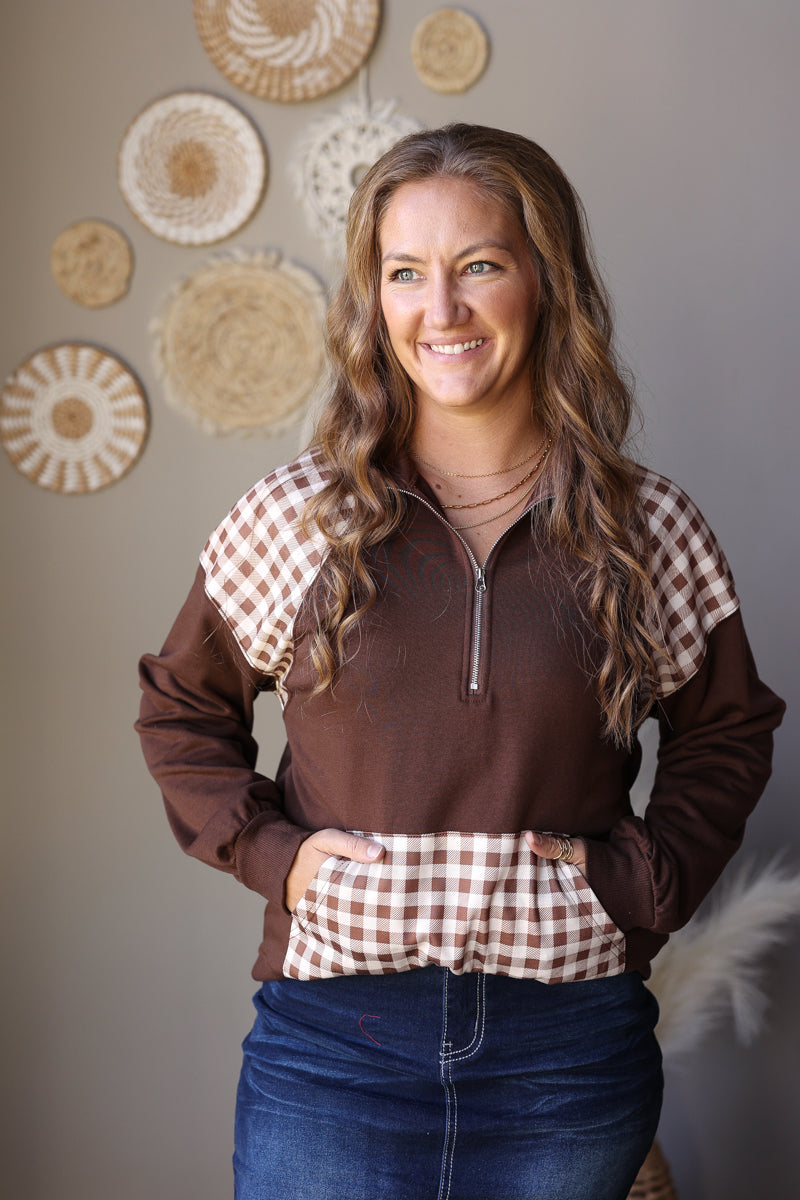 Front view of a brown quarter zip sweatshirt with plaid shoulder panels and a contrasting plaid pouch pocket.