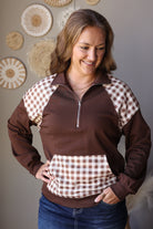 Brown quarter zip sweatshirt with hands in the plaid front pouch pocket, showing the collar and shoulder panels.