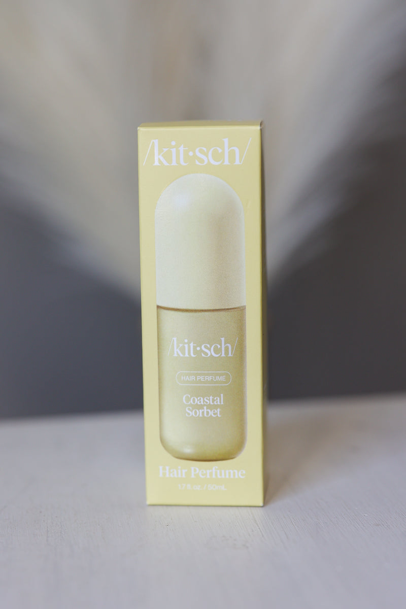 Kit-Sch Coastal Sorbet Hair Perfume in a pale yellow rectangular box with a matching bottle and cap, photographed against a soft gray and white blurred background.