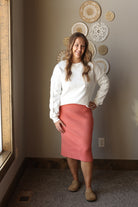 Woman in a white sweater and pink skirt standing in a room with decorative plates on the wall.