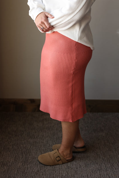 Person wearing a white sweater and pink ribbed skirt standing on a carpeted floor.