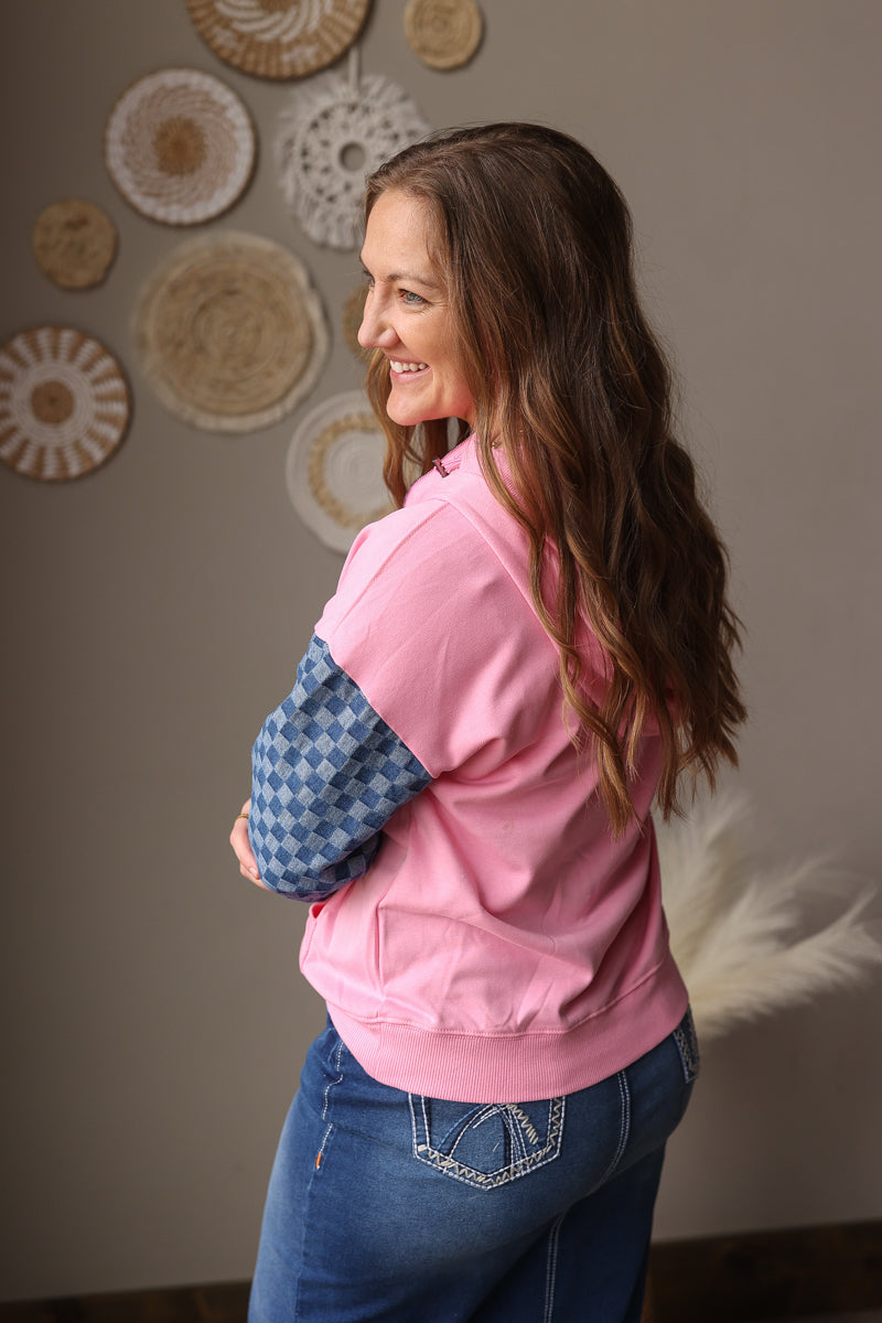Woman wearing a pink sweatshirt with blue denim checkered sleeves in a room with decorative plates on the wall.