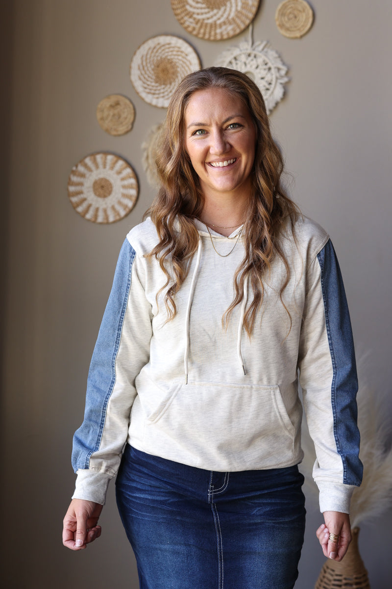 Angled front view of a light grey hoodie with contrasting blue denim sleeves and a drawstring hood.