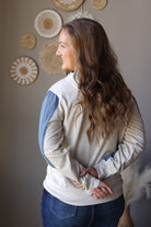 Back view of a light grey hoodie with a hood and contrasting blue denim sleeve panels.