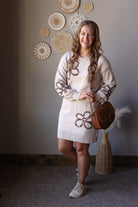 Full outfit view of a parchment floral sweater dress styled with tall brown boots and a round crossbody bag.