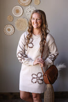 Front view of a parchment sweater dress with brown outlined flowers, puff sleeves, and a round brown bag.