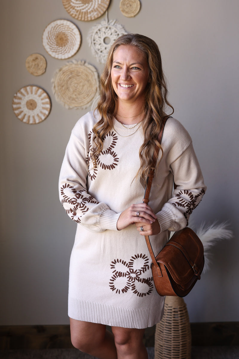 Front view of a parchment sweater dress with brown outlined flowers, puff sleeves, and a round brown bag.