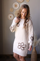 Close view of a parchment floral sweater dress highlighting its round neckline, puff sleeve, and flower details.