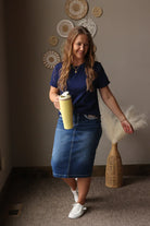 Woman holding a yellow water bottle and dried flowers in a room with decorative wall art.