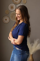 Woman wearing a blue shirt and jean skirt standing against a gray wall with decorative elements.
