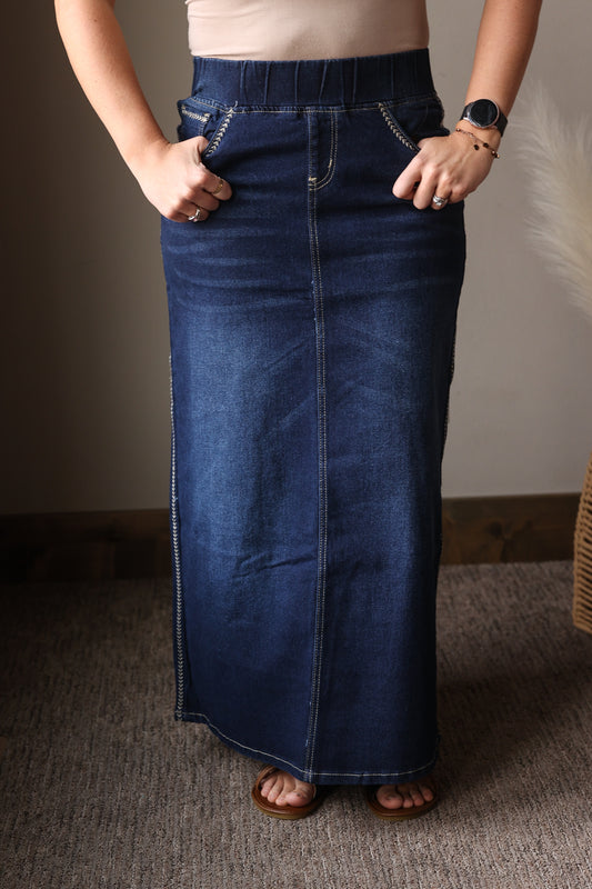 Person wearing a long blue denim skirt with a neutral background