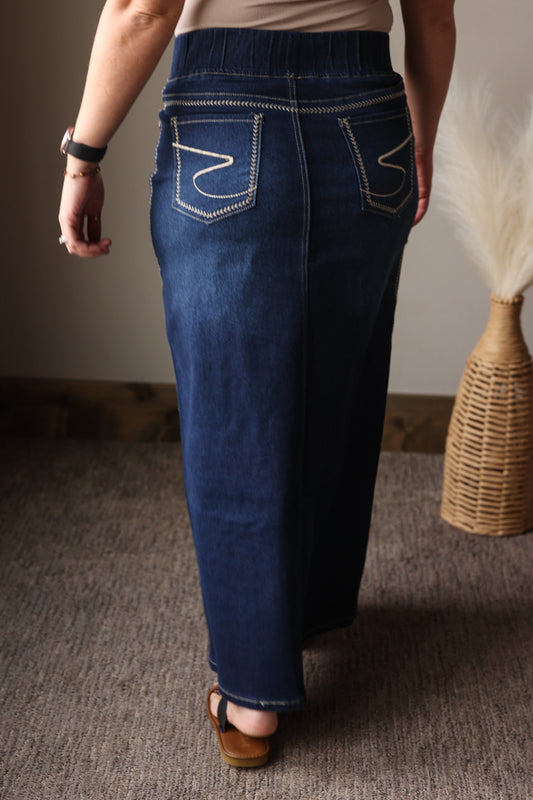 Person wearing blue jeans standing on a carpeted floor with a neutral wall and wicker basket in the background.