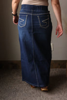 Person wearing a long blue denim skirt indoors.