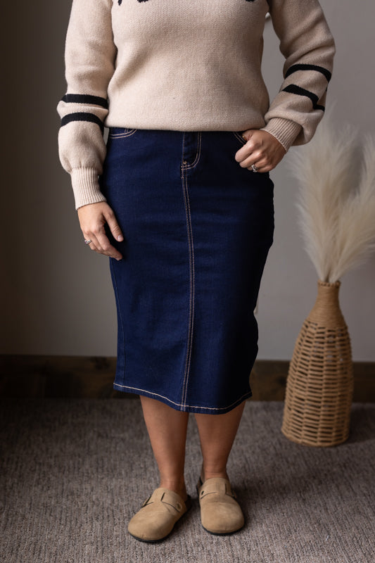 Person wearing a beige sweater with black stripes and a blue denim skirt, standing indoors for womens modest skirt fashion at classy closet.