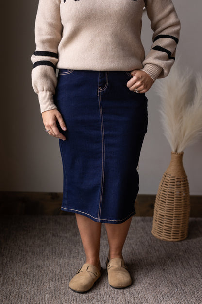 Person wearing a beige sweater with black stripes and a blue denim skirt, standing indoors for womens modest skirt fashion at classy closet.