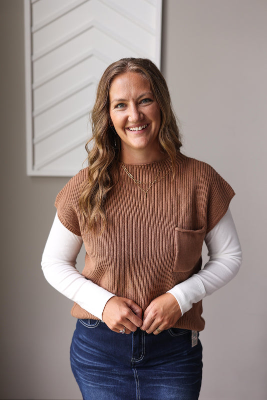 Woman wearing a brown ribbed vest over a white long-sleeve shirt with a neutral background