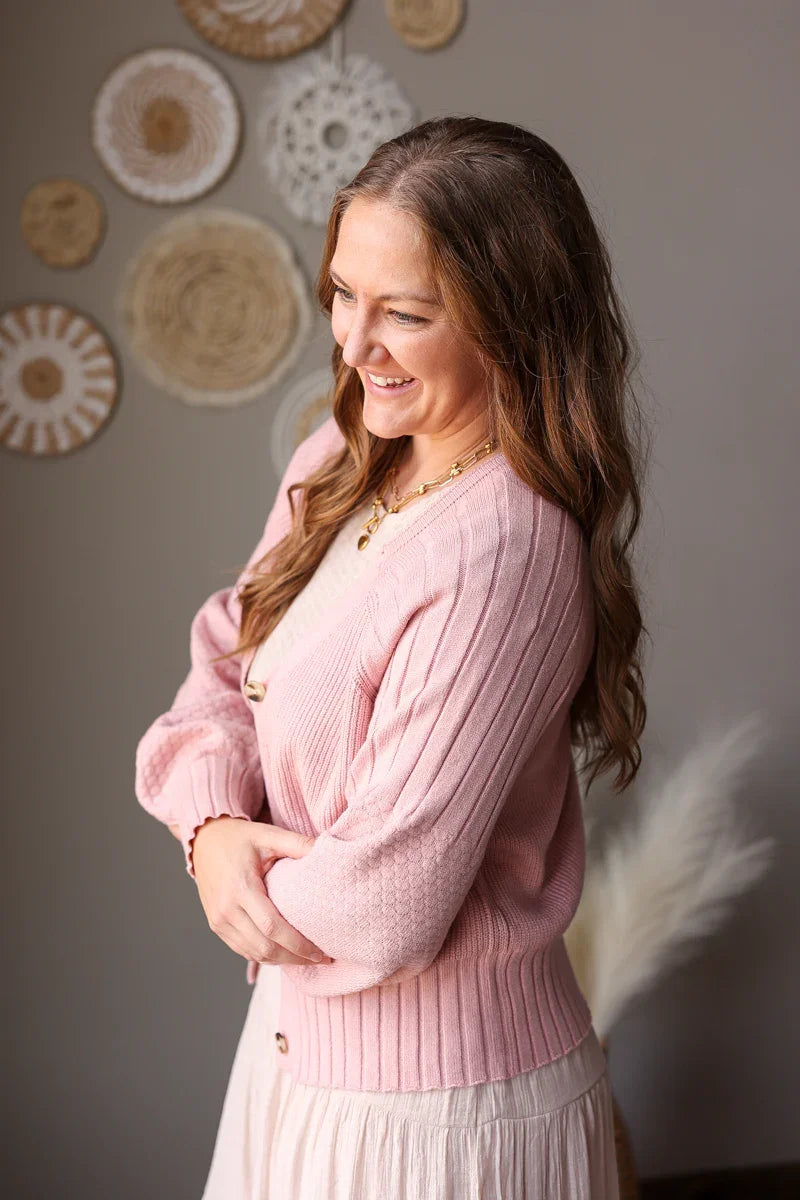 Woman wearing a pink sweater standing in front of decorative wall art.