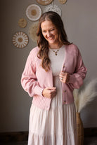Woman wearing a pink cardigan and white dress in a room with decorative wall art.
