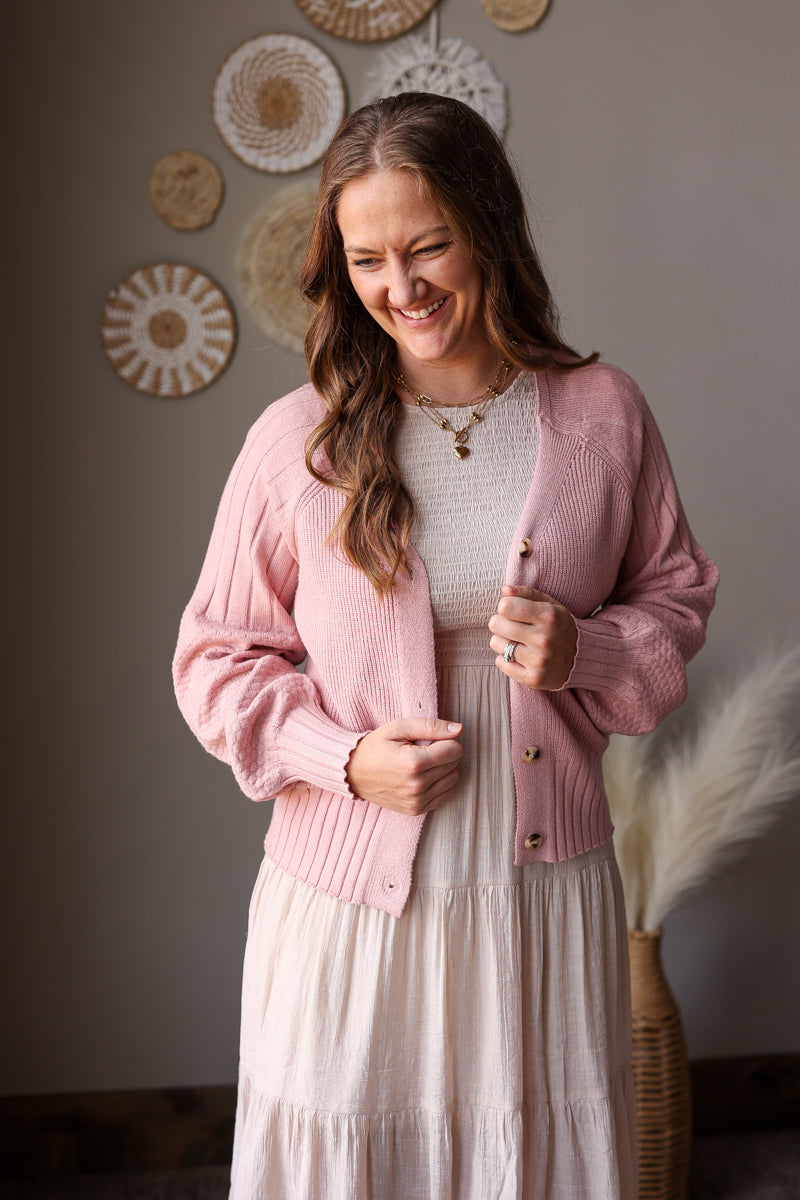 Woman wearing a pink cardigan and white dress in a room with decorative wall art.