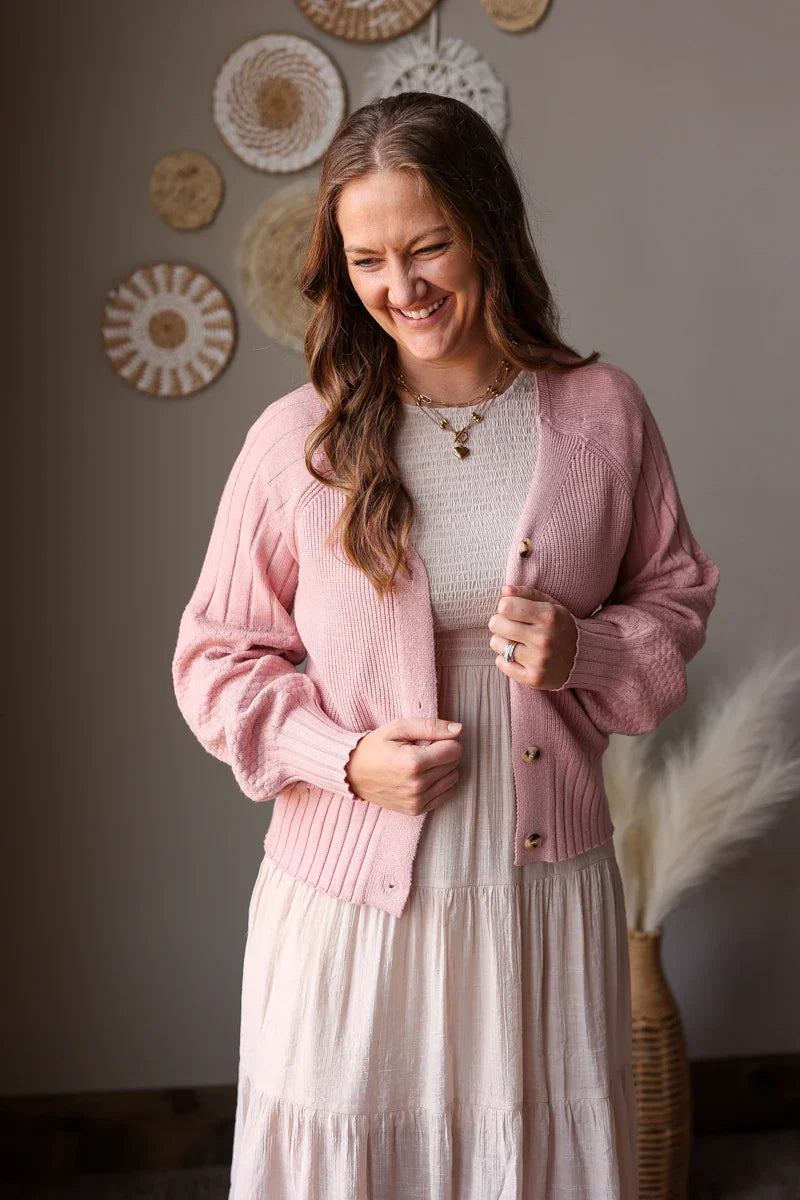 Woman wearing a pink cardigan and white dress in a room with decorative wall art.