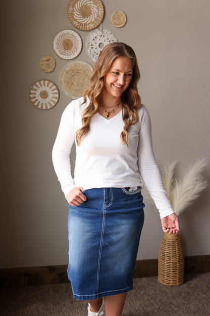 Woman wearing a white long-sleeve shirt and blue denim skirt standing in a room with decorative wall art.