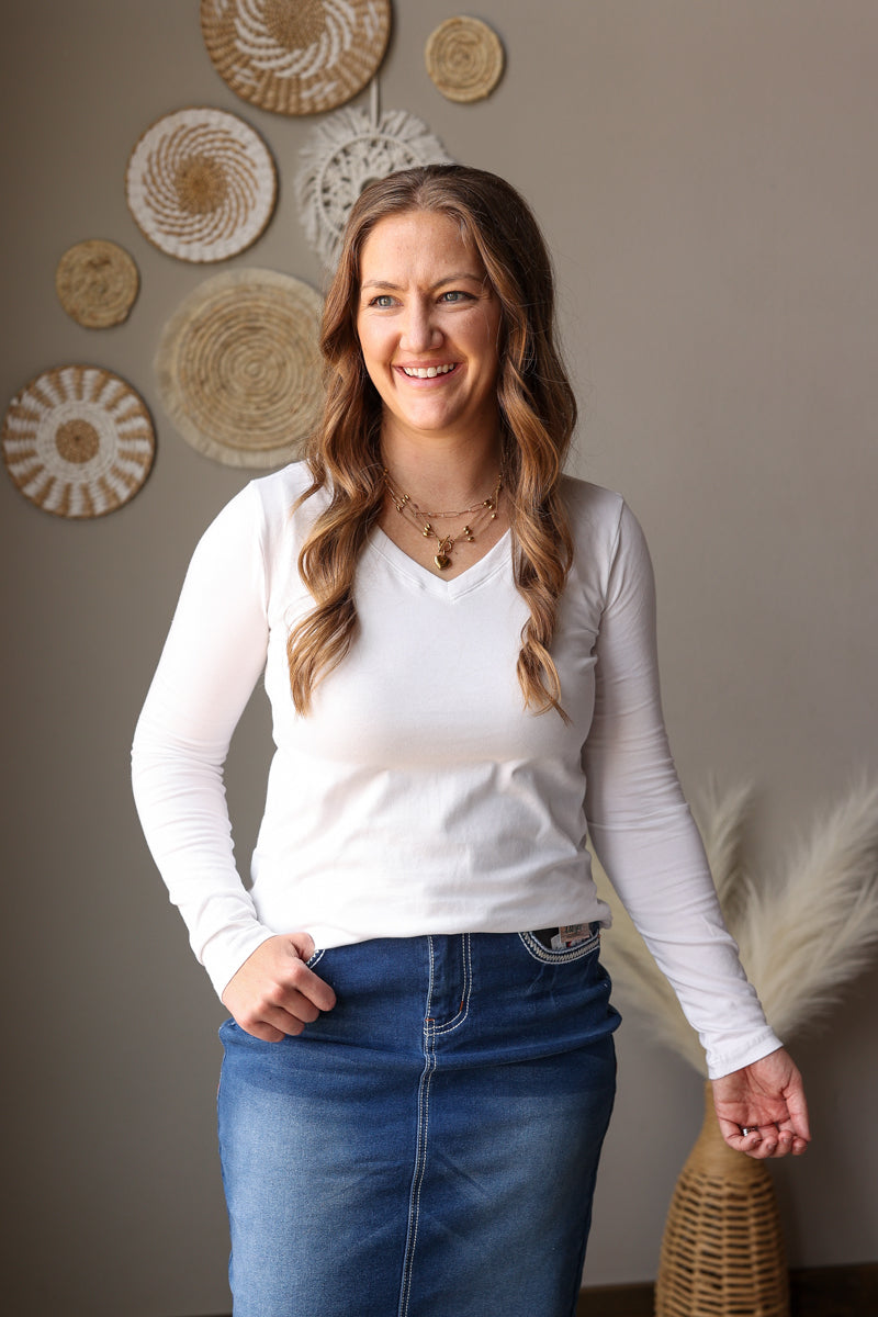Woman wearing a white long-sleeve top and blue jeans standing in front of decorative wall art.