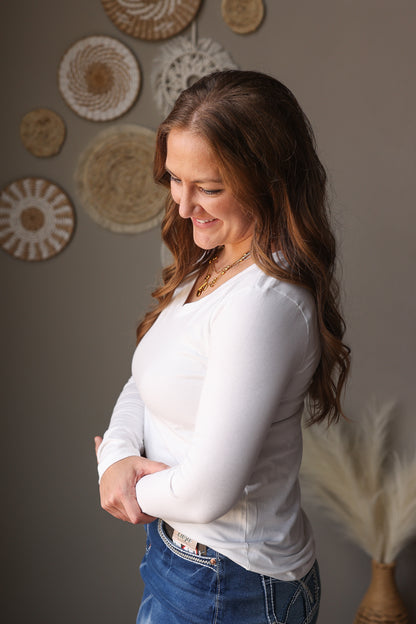 Woman wearing a white long-sleeve shirt and blue jean skirt standing against a wall with decorative plates.