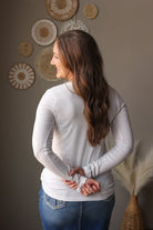 Woman wearing a white long-sleeve shirt and blue jean skirt standing in front of decorative wall art.