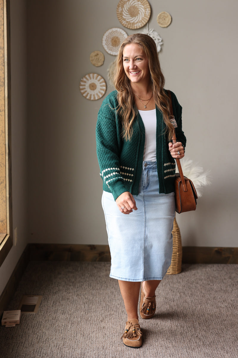 Full-length front view of an emerald textured cardigan worn open with a light denim skirt and brown boots.