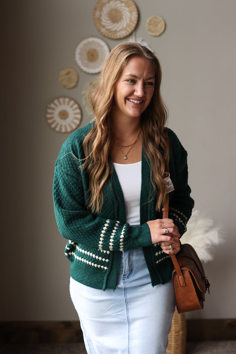 Close front view of an emerald diamond stripe cardigan worn open over a white top with a brown crossbody bag.