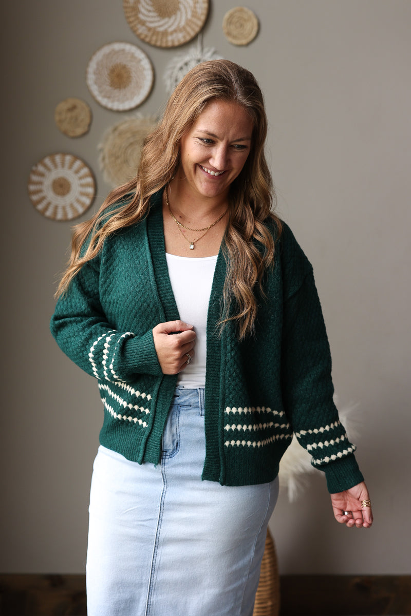 Front close-up of an emerald cardigan highlighting its textured knit, cream diamond stripes, and ribbed trim.