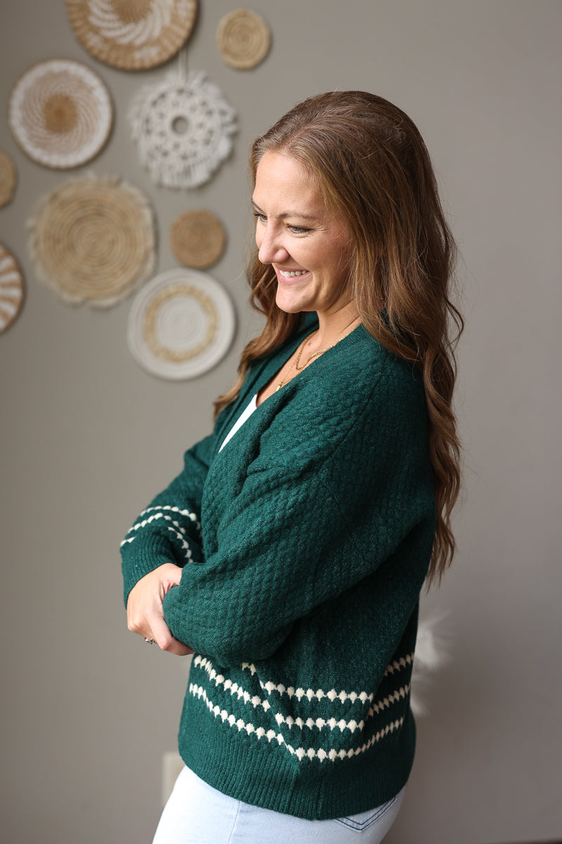 Side view of an emerald knit cardigan showing cream patterned stripes at the cuff and hem.