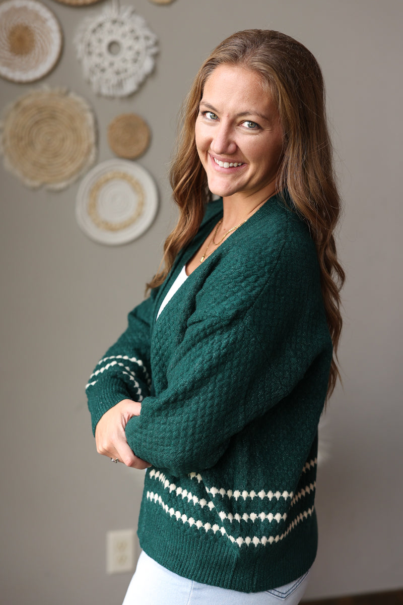 Side close-up of an emerald green cardigan showing the cream patterned cuff and matching hem stripes.